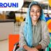 Estudante sorrindo em cadeira de rodas, com cabelo azul, ao fundo ambiente de universidade com logo do Prouni. Imagem: Gov.br