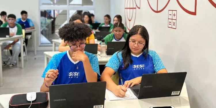 Alunos do SESI Amapá em aula utilizando laptops e material de apoio.