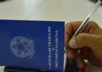Mão segurando uma carteira de trabalho enquanto preenche informações com uma caneta.