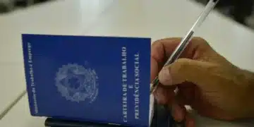 Mão segurando uma carteira de trabalho enquanto preenche informações com uma caneta.