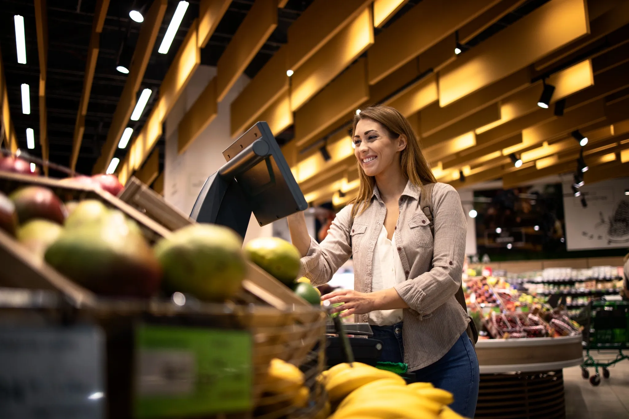 Cliente sorridente utilizando a balança digital para pesar frutas no supermercado.