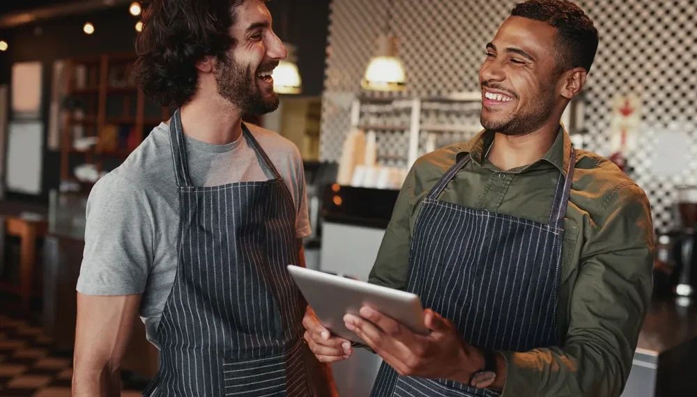 Dois profissionais sorrindo enquanto olham para um tablet na cozinha de um restaurante.