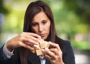 Mulher concentrada montando um quebra-cabeça de madeira, representando raciocínio lógico e alta inteligência.