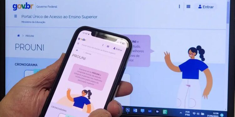 Pessoa segurando celular com a página do Prouni aberta, em frente a um computador mostrando a mesma página. Imagem: Agência Gov