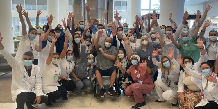 Equipe de profissionais de saúde e paciente sorrindo em ambiente hospitalar, com todos levantando as mãos em celebração.