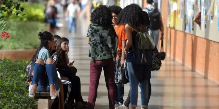 Grupo de estudantes interagindo no corredor da escola, com alguns sentados e outros em pé.