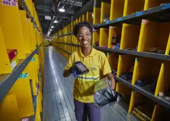Funcionária sorridente organizando pacotes em centro logístico com prateleiras amarelas.