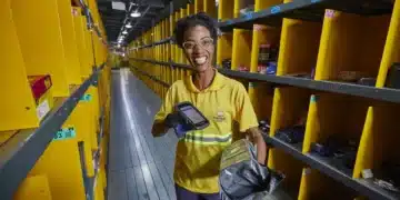Funcionária sorridente organizando pacotes em centro logístico com prateleiras amarelas.