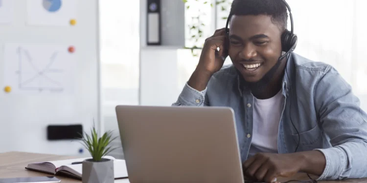 Homem sorrindo enquanto trabalha em um laptop com fones de ouvido.