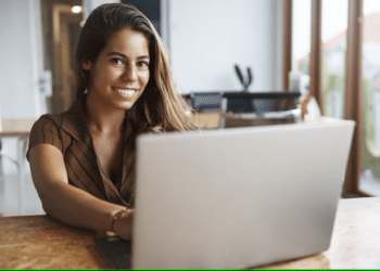 Mulher sorrindo enquanto trabalha em um laptop em ambiente moderno e iluminado.