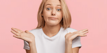 Mulher com expressão de dúvida, fazendo um gesto de encolher os ombros, com fundo rosa.