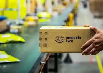 Pacote do Mercado Livre sendo manuseado em centro logístico, com esteira e pacotes ao fundo
