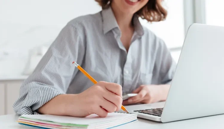  Mulher fazendo anotações enquanto estuda no laptop.