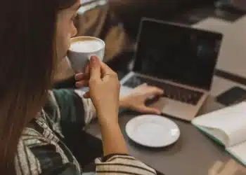 Mulher tomando café enquanto trabalha no laptop em uma cafeteria.