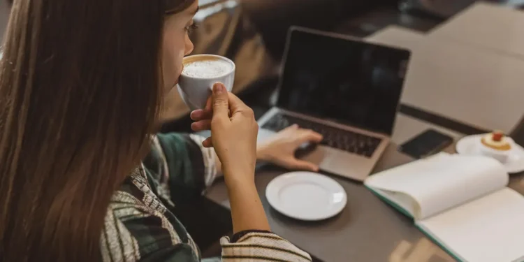 Mulher tomando café enquanto trabalha no laptop em uma cafeteria.