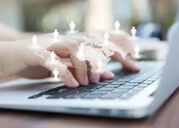 Mãos digitando em um notebook com ícones de conexões digitais representando networking global.