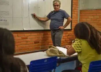 Professor explicando conteúdo no quadro para alunos em sala de aula.
