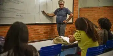 Professor explicando conteúdo no quadro para alunos em sala de aula.