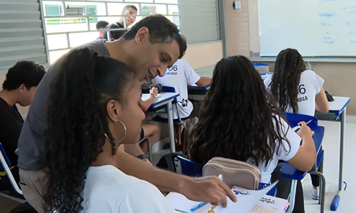 Professor auxiliando aluna em sala de aula durante uma explicação.