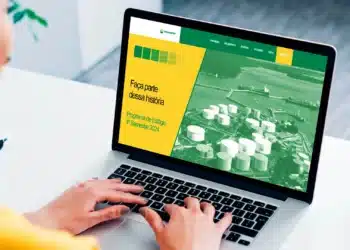 Pessoa utilizando um laptop para acessar o site do Programa de Estágio da Transpetro, com fundo de área industrial.