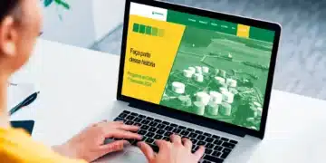 Pessoa utilizando um laptop para acessar o site do Programa de Estágio da Transpetro, com fundo de área industrial.