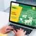 Pessoa utilizando um laptop para acessar o site do Programa de Estágio da Transpetro, com fundo de área industrial.