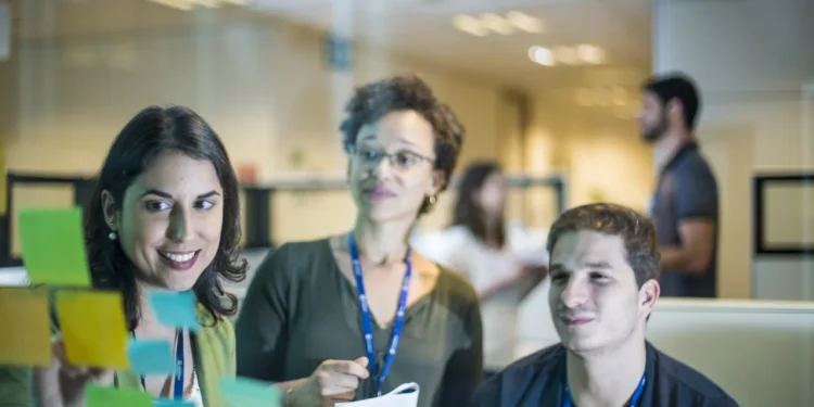 Equipe de trabalho colaborando em um escritório, organizando ideias com post-its em um quadro.