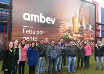 Funcionários da Ambev posando sorridentes em frente a um grande painel institucional com a frase "Feita por gente apaixonada."