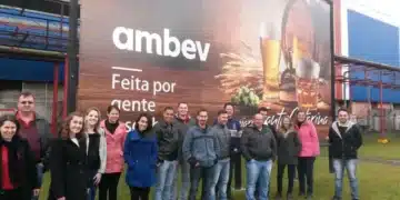 Funcionários da Ambev posando sorridentes em frente a um grande painel institucional com a frase "Feita por gente apaixonada."