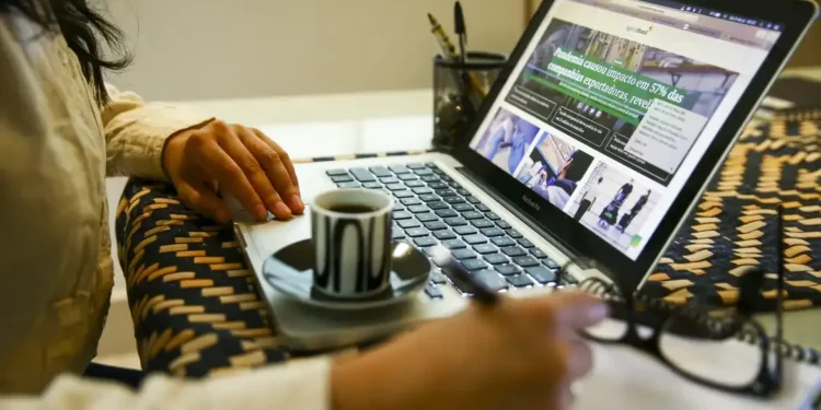 Pessoa trabalhando no laptop com uma xícara de café.