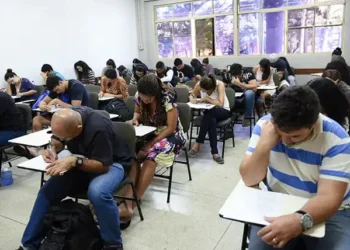 Grupo de estudantes em uma sala de aula realizando uma prova em carteiras individuais.
