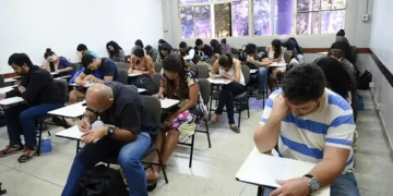 Grupo de estudantes em uma sala de aula realizando uma prova em carteiras individuais.