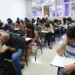 Grupo de estudantes em uma sala de aula realizando uma prova em carteiras individuais.