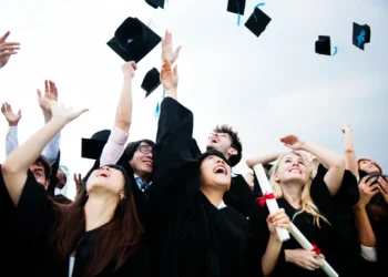 Formandos celebrando a conclusão da faculdade de 2 anos; lançando chapéus para o alto.