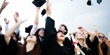 Formandos celebrando a conclusão da faculdade de 2 anos; lançando chapéus para o alto.