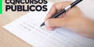 Mão segurando uma caneta enquanto preenche um cartão-resposta de prova objetiva, representando a realização de concursos públicos.