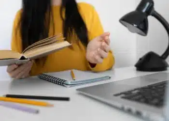 Estudante com livro e laptop, se preparando para o ENEM 2025 com apoio de curso online gratuito de redação.