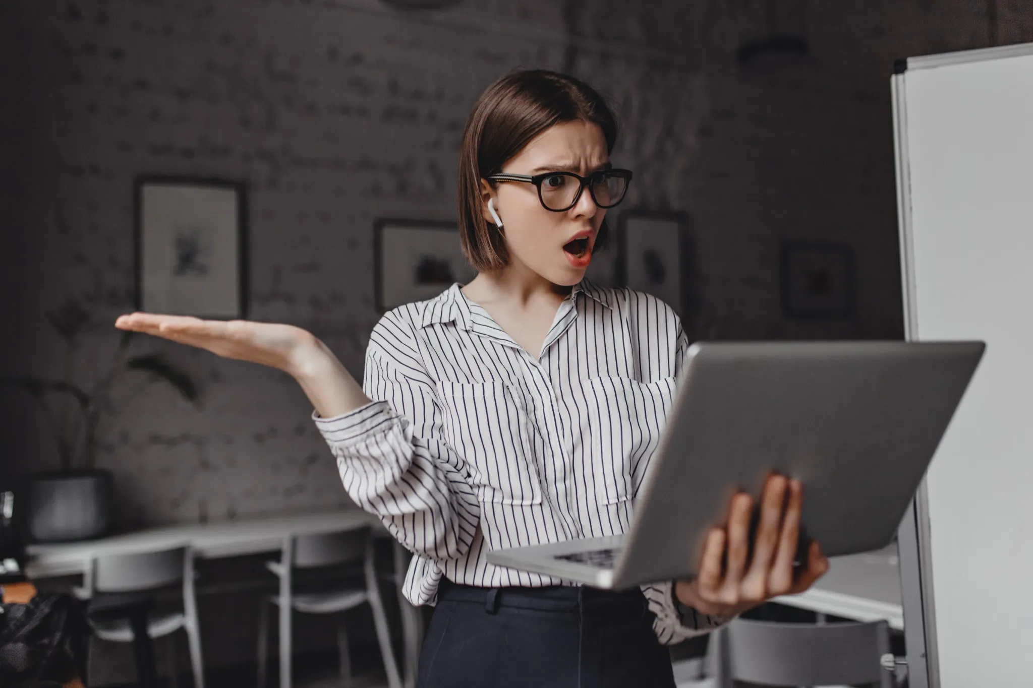  Mulher com expressão de frustração segurando um notebook e gesticulando em um escritório.