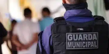 : Guarda Municipal de costas em patrulha, observando um grupo de pessoas à frente.