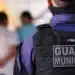 : Guarda Municipal de costas em patrulha, observando um grupo de pessoas à frente.