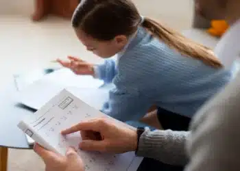 Criança estudando matemática em casa com ajuda de um adulto.