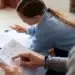 Criança estudando matemática em casa com ajuda de um adulto.