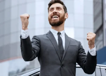 Homem de terno comemorando com expressão de sucesso em frente a um prédio moderno.