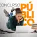 Mulher estudando para concurso público com laptop e livros ao redor.