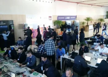Evento de tecnologia e startups com participantes trabalhando em laptops e networking.