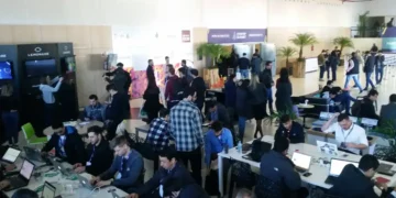 Evento de tecnologia e startups com participantes trabalhando em laptops e networking.
