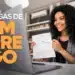 Mulher sorridente segura um contrato de trabalho durante uma entrevista online, com um notebook à sua frente e a frase "Vagas de Emprego" destacada na tela.