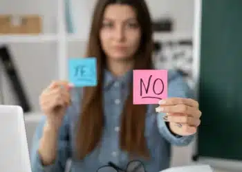 Mulher segurando dois papéis, um azul com "YES" e um rosa com "NO", simbolizando indecisão ou escolhas no trabalho.