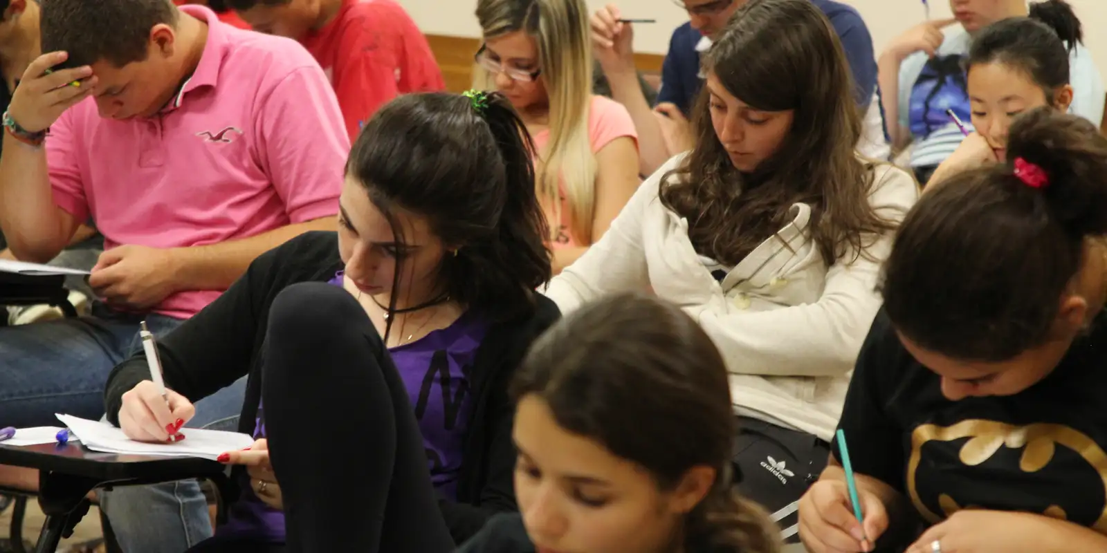 Estudantes concentrados respondendo a uma prova em uma sala de exame.