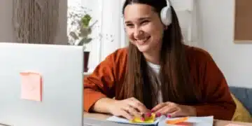 Pessoa sorrindo enquanto estuda em casa com fones de ouvido e usando post-its coloridos para organizar suas anotações.